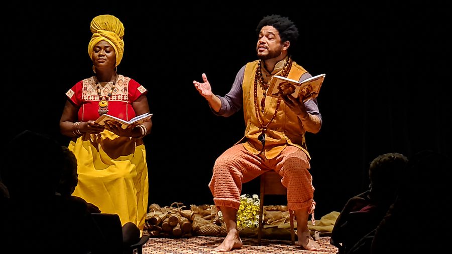 Contadores de histórias sentados no palco, com livros nas mãos, durante a apresentação de O Menino Rei e a Menina Rainha
